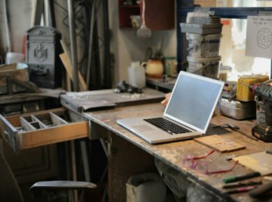 From above of modern laptop laying at table among different tools and equipment in workshop